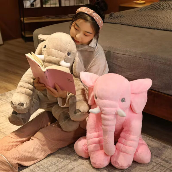 Baby Elephant Stuffed Animal A woman reading a book while carrying a grey baby elephant stuffed animal. A pink stuffed animal elephant is sitting beside her.