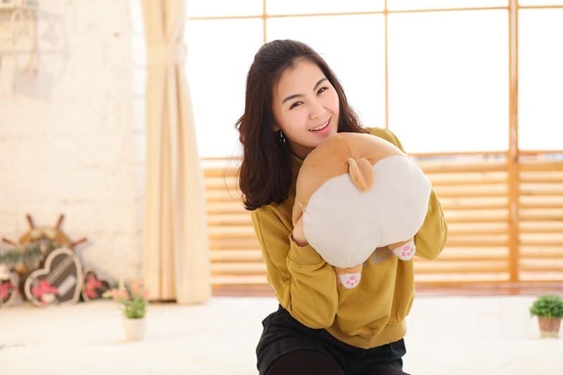 woman holding a corgi butt plush pillow