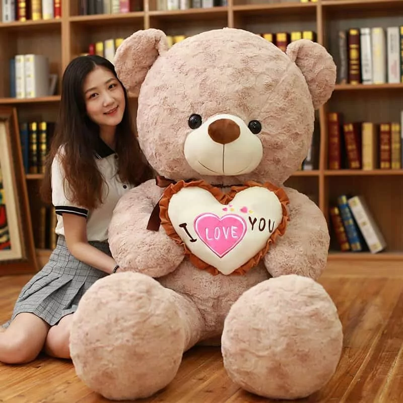 Woman sitting beside a 100 cm giant light-pink teddy bear holding an i love you pillow