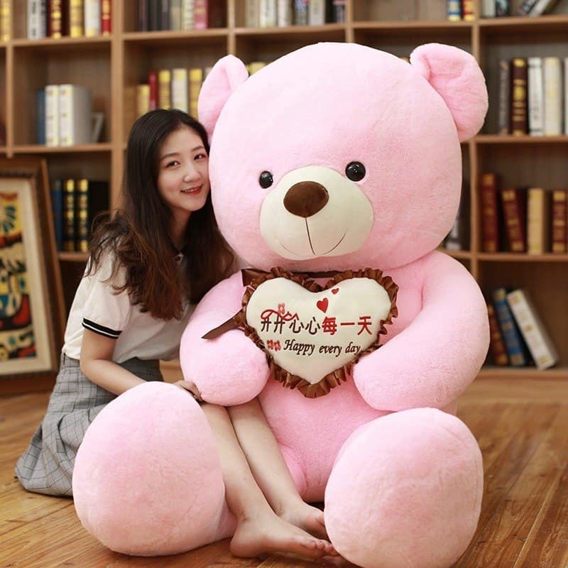 Woman sitting beside a 100 cm giant pink teddy bear holding an i love you pillow