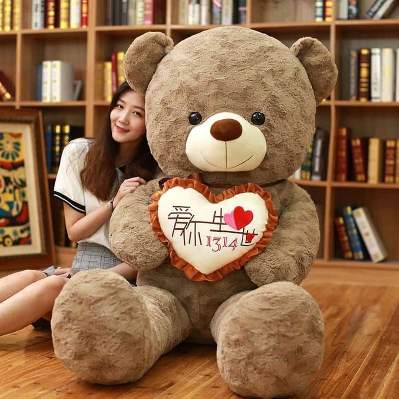Woman sitting beside a 100 cm giant light-brown teddy bear holding an i love you pillow