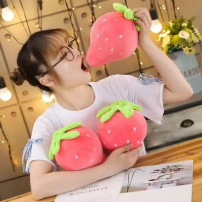 Woman holding two cute strawberry pillow and eating one strawberry plushie