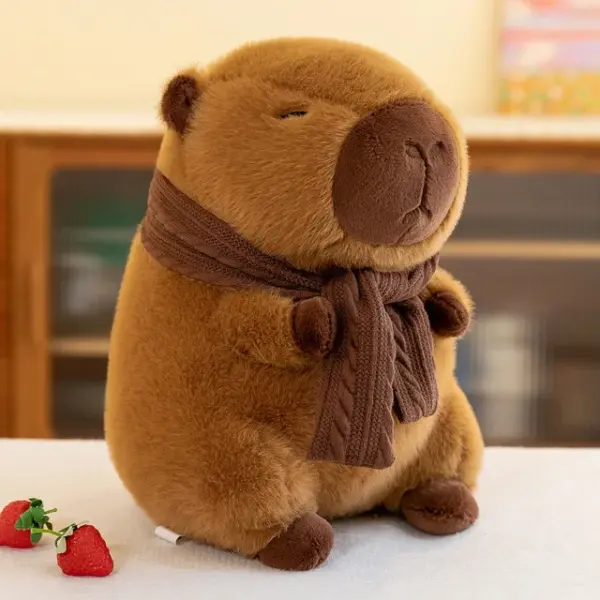 A 35cm brown capybara plush wearing a knitted scarf, sitting on a white surface with strawberries nearby