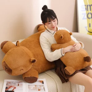 A person hugging a medium-sized giant capybara plush while a larger plush rests on a chair in the background.