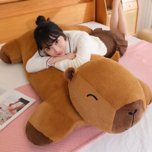 A person lounging on a giant capybara plush placed on a bed, showcasing its use as a relaxing and oversized pillow.