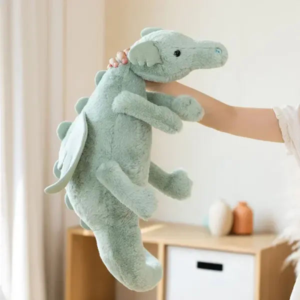 A soft green dragon stuffed animal being held up by a person in a bright, cozy room.